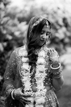 A bride adorned in traditional Indian attire with intricate henna, captured outdoors in black and white.