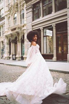 Elegant bride in a lace gown twirls on a charming cobblestone street, showcasing urban romance.