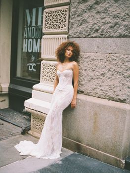 Stylish bride in a lace wedding dress posing against a textured city wall.
