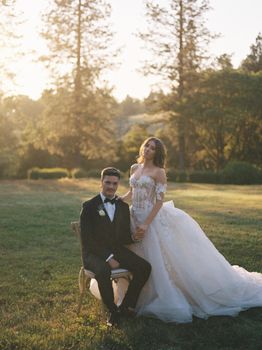 Bride and groom in formal attire posing outdoors during sunset amid nature.