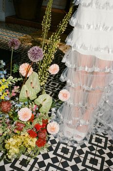 Elegant ruffled dress alongside vibrant floral bouquet on patterned tiles.