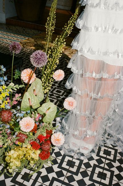 Elegant ruffled dress alongside vibrant floral bouquet on patterned tiles.