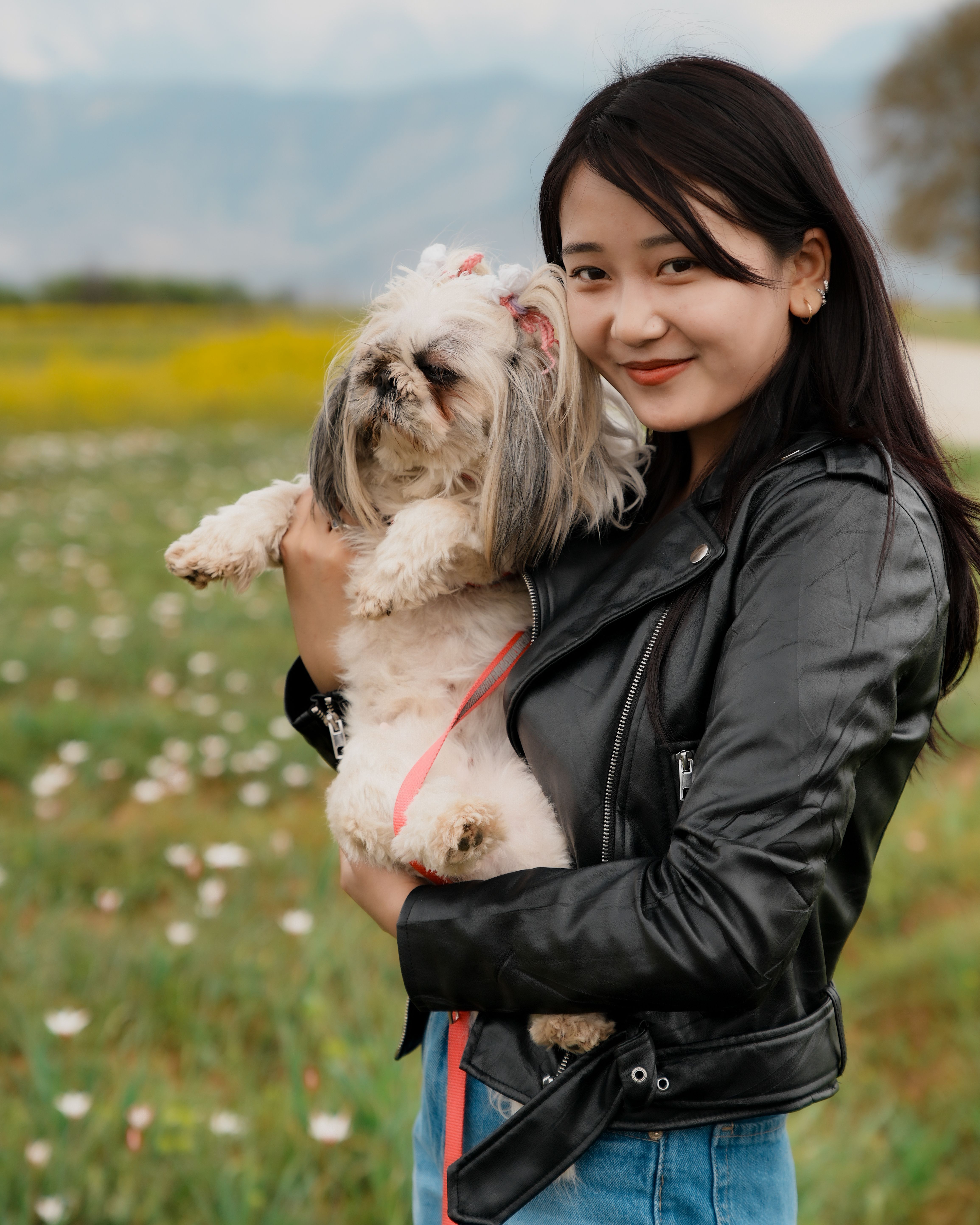 Happy woman enjoying a sunny day outdoors while holding her Shih Tzu dog in a colorful field.