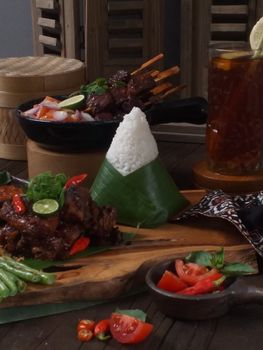 Delicious Indonesian meal featuring satay, rice, fresh vegetables, and iced tea.