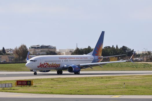 Jet2holidays airplane taxiing on a sunlit runway in a city airport setting.