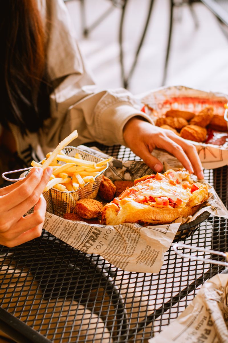 Close-up of a casual meal with french fries, sandwich, and snacks on a metal table.