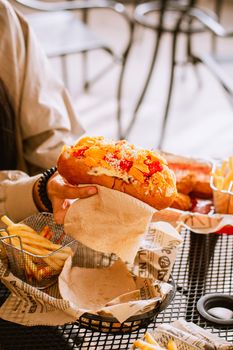 A delicious hot dog with toppings held over a table with fries, creating an appetizing scene.
