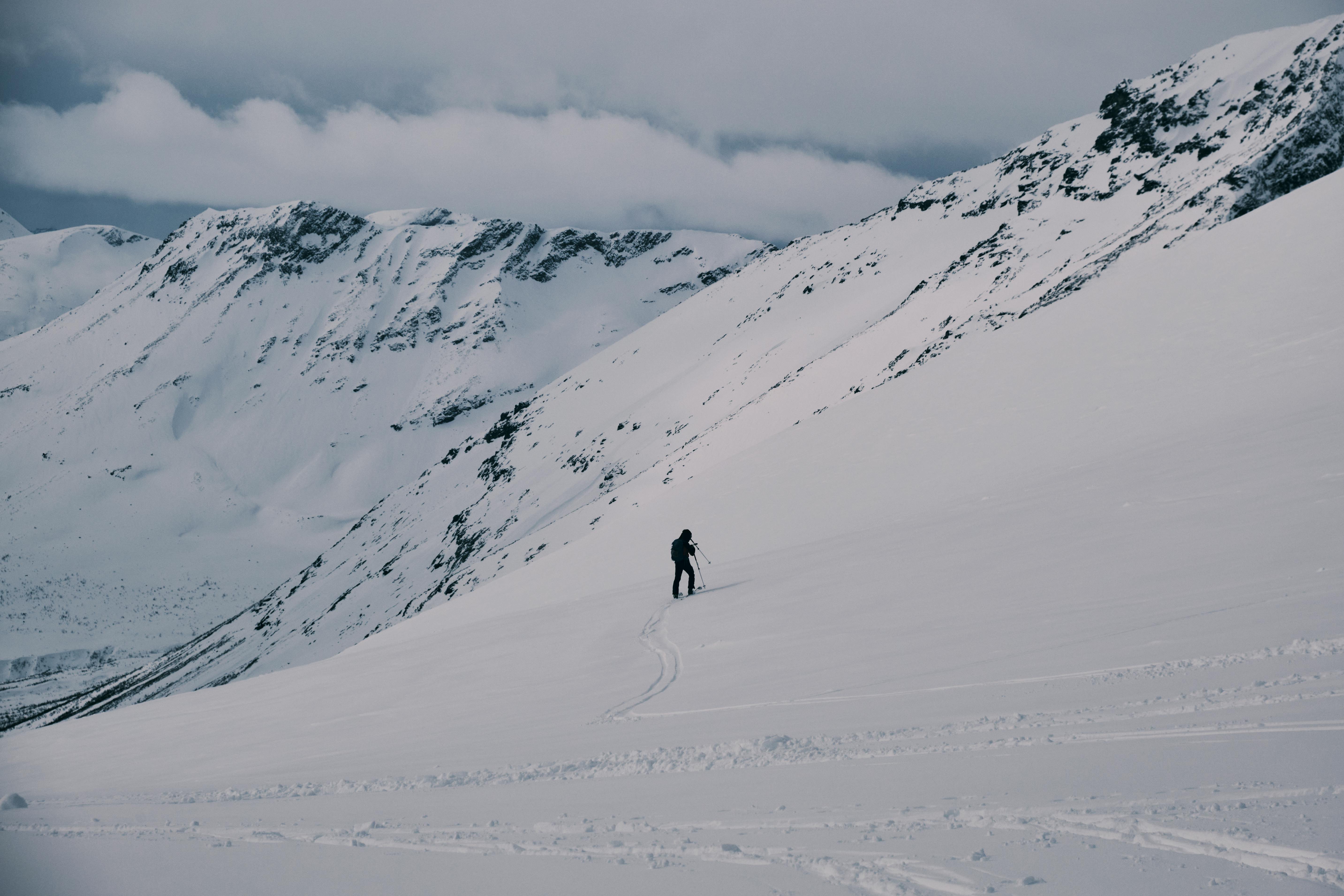A lone skier traversing a vast, snow-covered mountain range under a cloudy sky.
