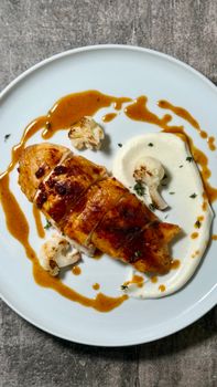 Deliciously plated roast chicken breast with savory sauce and cauliflower puree.