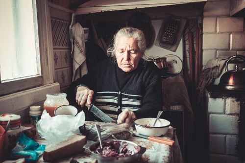 Free Senior woman cutting vegetables in a vintage kitchen setting, creating a homely and nostalgic atmosphere. Stock Photo