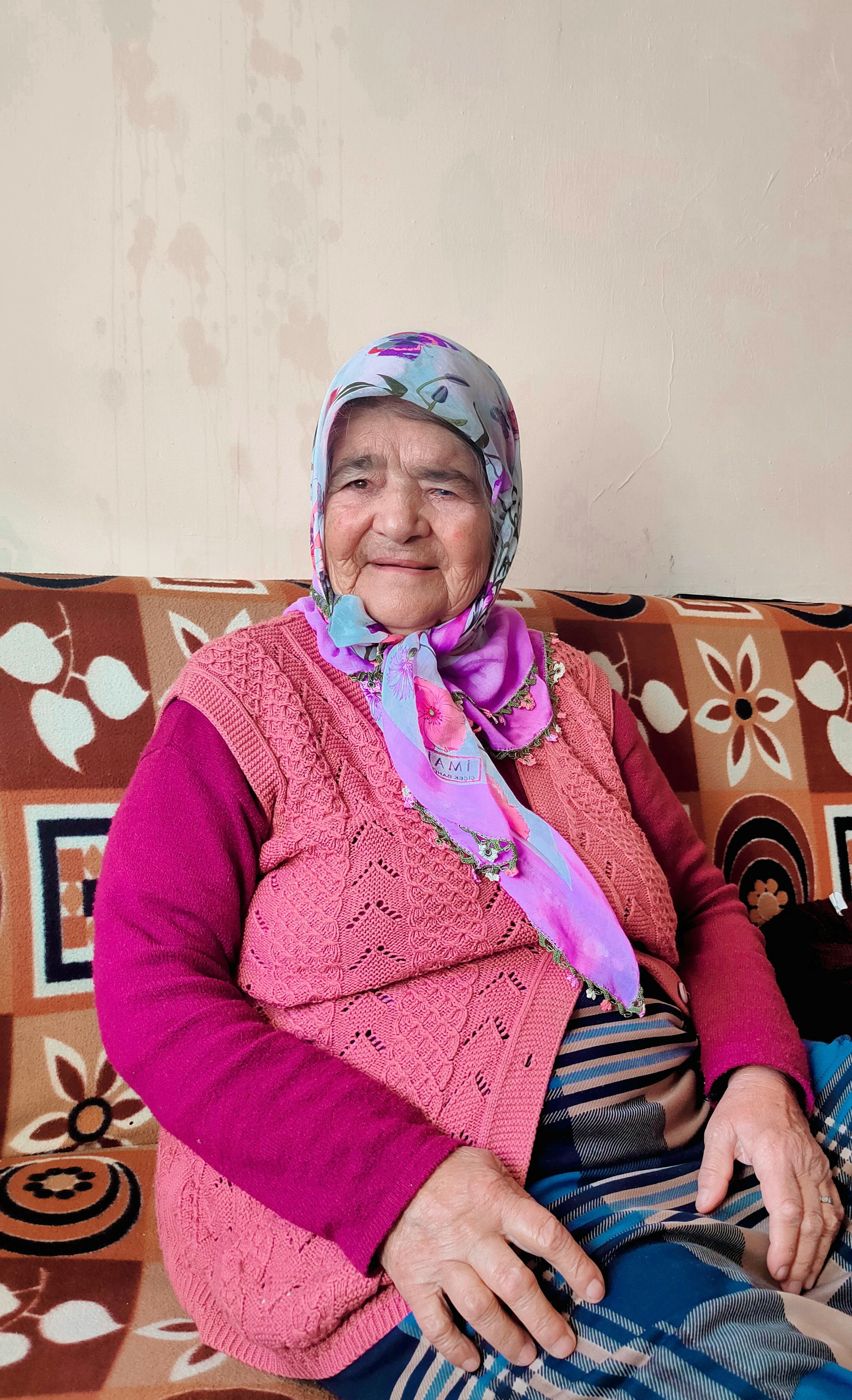 Cheerful elderly woman in colorful attire sitting on a patterned sofa indoors.