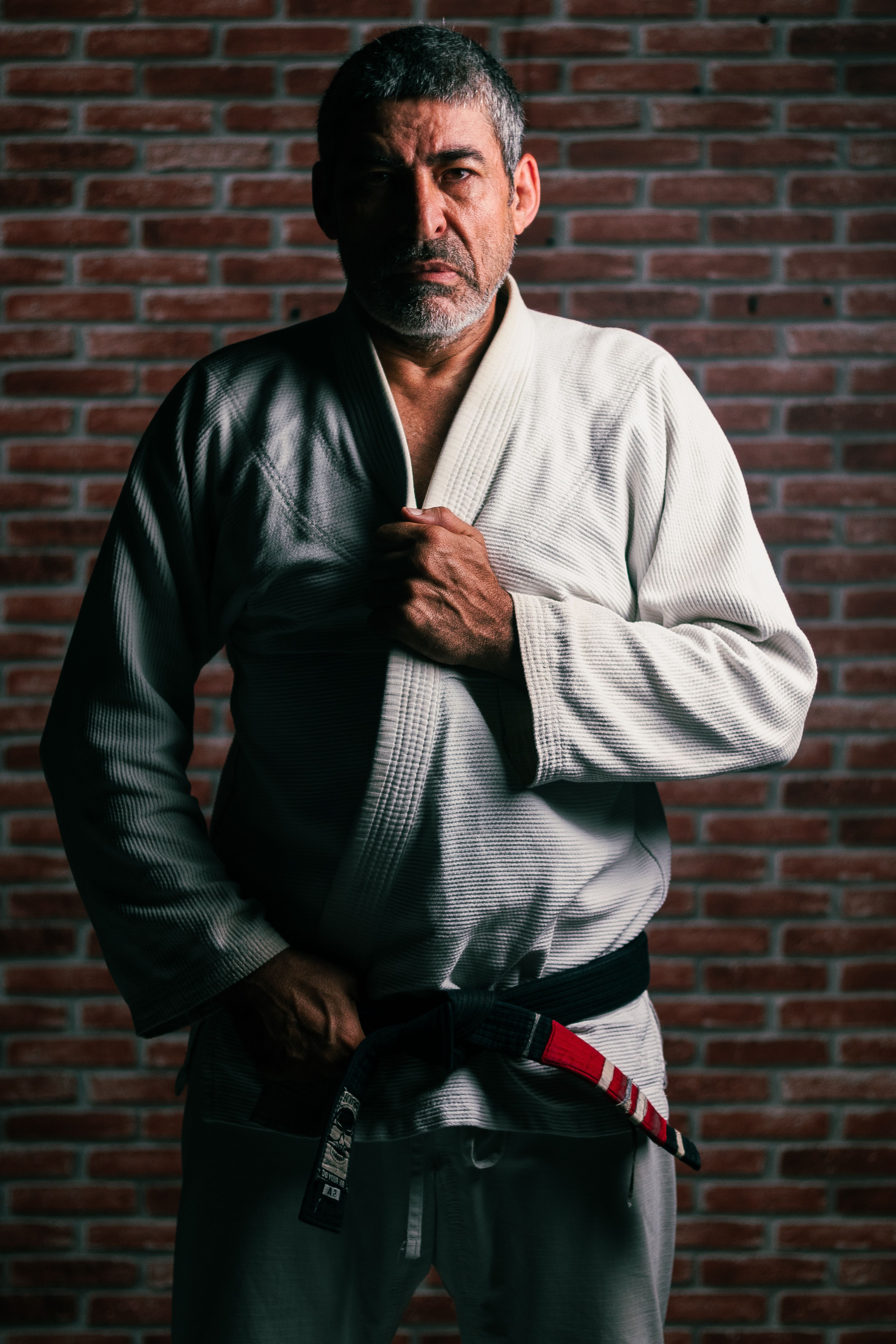 Portrait of a martial artist wearing a gi, standing confidently against a brick wall.
