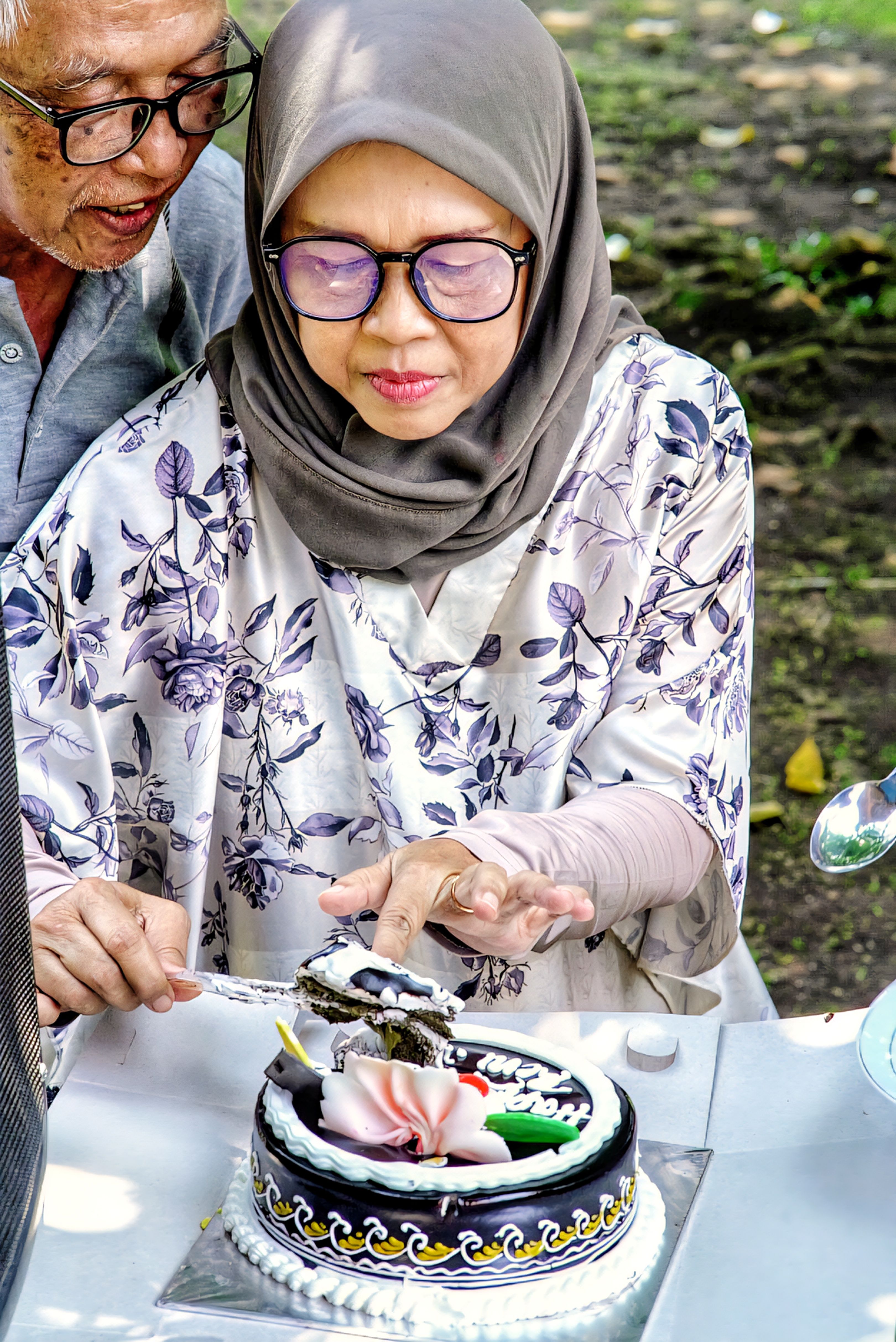 Senior couple cutting a cake outdoors in West Java, Indonesia, enjoying a special occasion.