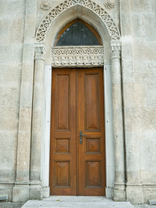 Free A detailed view of a wooden door set within an ornate stone archway, showcasing historical architecture. Stock Photo