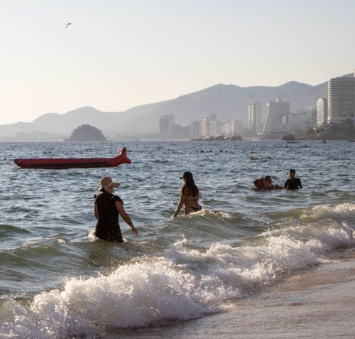Free Sunlit scene of tourists enjoying Acapulco's beach with city skyline view. Stock Photo
