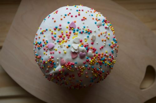 Free Top view of a cake covered with white frosting and colorful sprinkles on a wooden board. Stock Photo