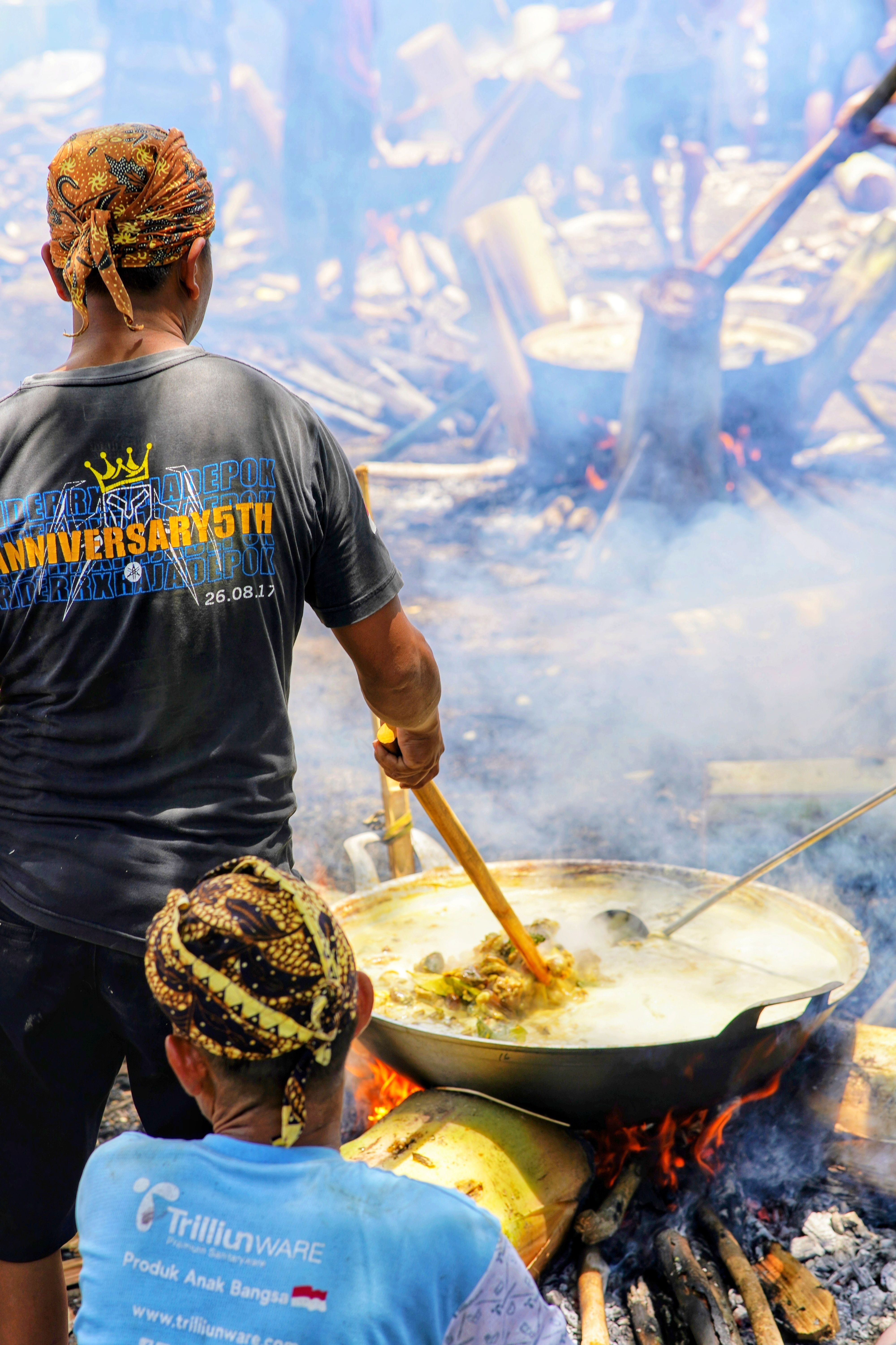 Men cooking outdoors in Central Java, Indonesia at a traditional event with large woks.