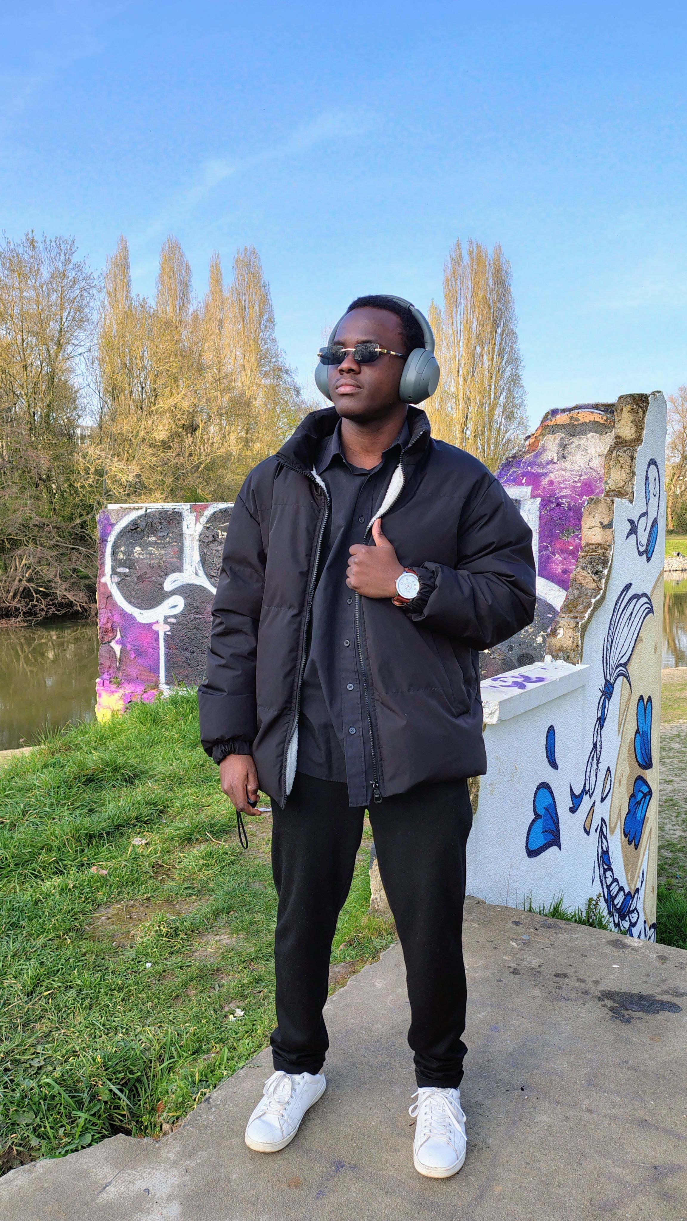 Fashionable young man wearing headphones stands by a colorful graffiti wall outdoors.