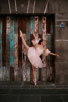 Elegant ballerina in pink dress poses on a rustic street in Mexico.