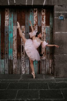 Ballerina in a pink dress showcasing elegance against a weathered wooden door in Puebla, Mexico.
