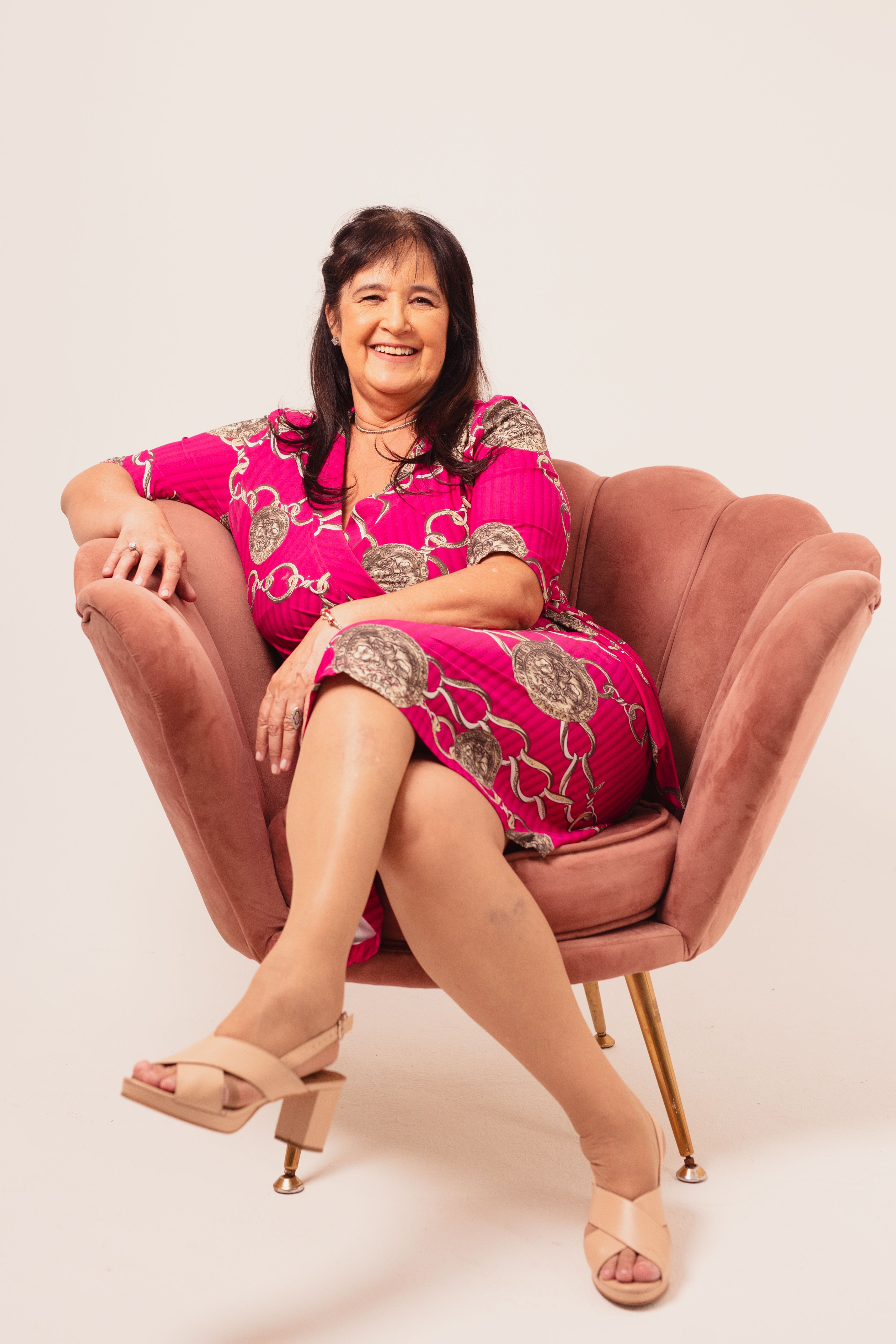 Smiling woman in a vibrant pink dress sitting comfortably in a stylish armchair.