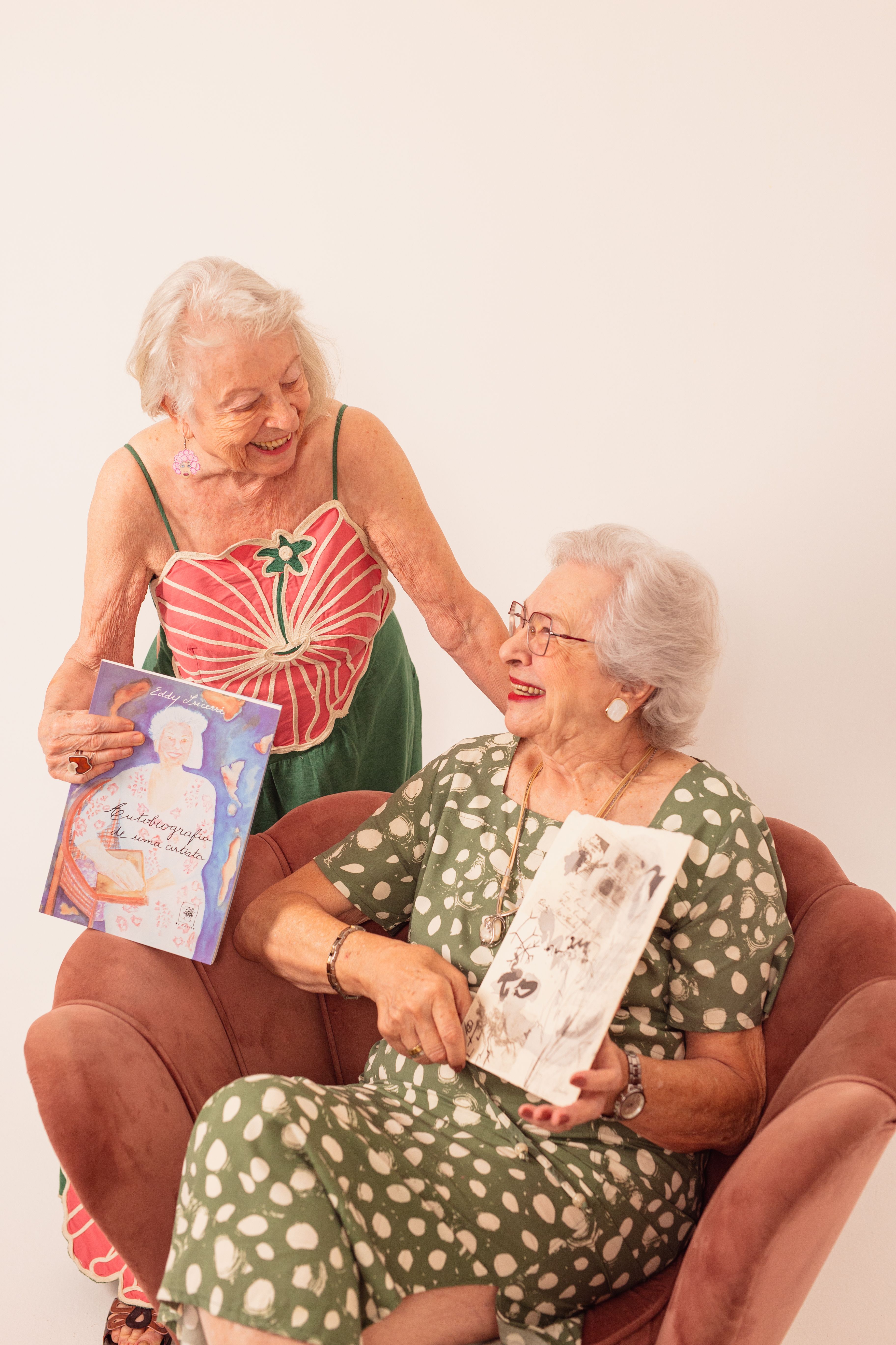 Two happy senior women sharing and enjoying art books indoors, fostering friendship.