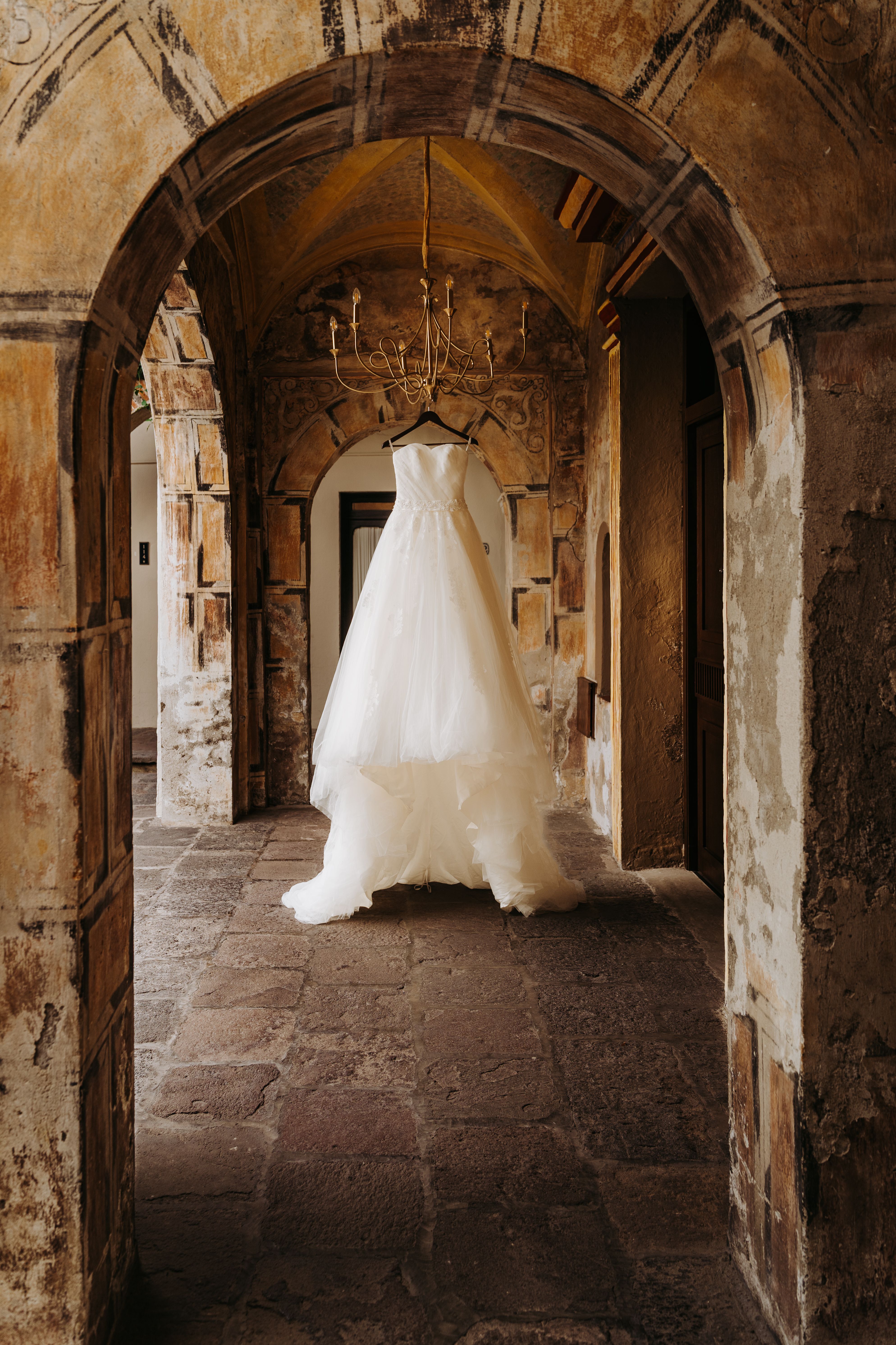 A beautiful wedding dress hanging in a rustic stone archway.