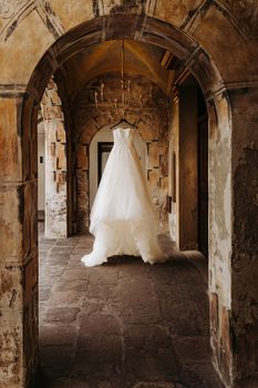 A beautiful wedding dress hanging in a rustic stone archway.