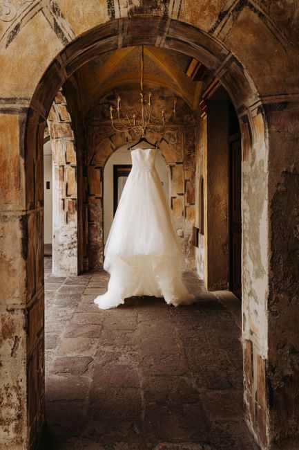A beautiful wedding dress hanging in a rustic stone archway.