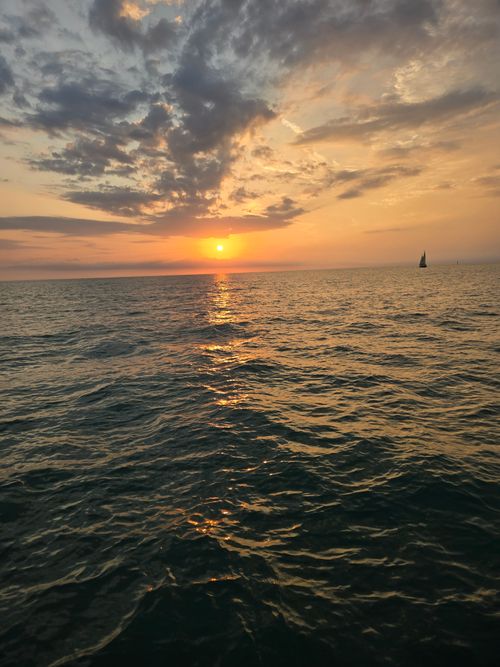 Free A breathtaking sunset casts a warm glow over the expansive ocean as clouds create a dramatic sky. Stock Photo
