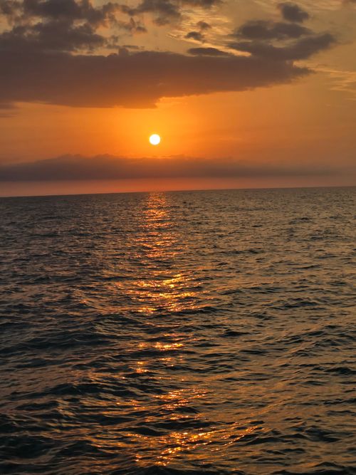 Free Beautiful sunset over the ocean with dramatic clouds and shimmering water reflections. Stock Photo