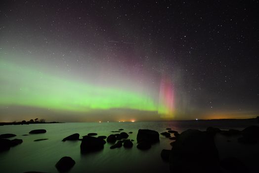 Vibrant aurora borealis illuminates the night sky over a rocky beachfront in Estonia. A breathtaking natural spectacle.
