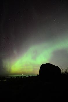 Captivating view of the Northern Lights illuminating the night sky over a rocky shore.