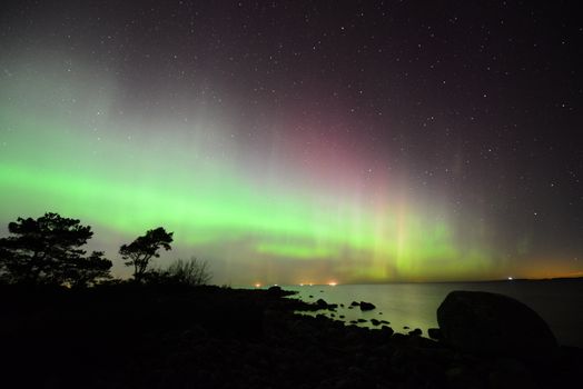 Mesmerizing view of the aurora borealis illuminating a rocky shoreline under a starry sky.