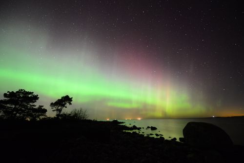 Free Mesmerizing view of the aurora borealis illuminating a rocky shoreline under a starry sky. Stock Photo