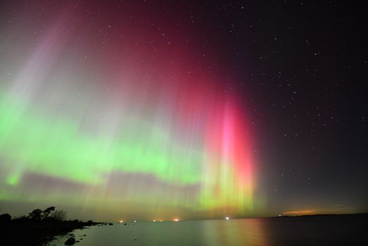 Mesmerizing aurora borealis lights up the night sky in vibrant hues over a calm lake shore.