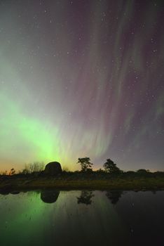 Enchanting view of aurora borealis mirrored in tranquil water under a starry sky.