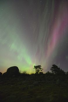 Beautiful aurora borealis dancing over a rocky landscape under a starry night sky.