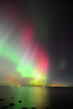 Vibrant Northern Lights reflecting on a tranquil sea under a starlit sky.