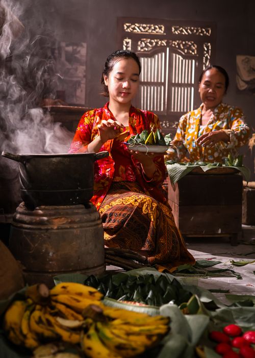 Free Women preparing traditional dishes in a Southeast Asian kitchen with steam rising. Stock Photo