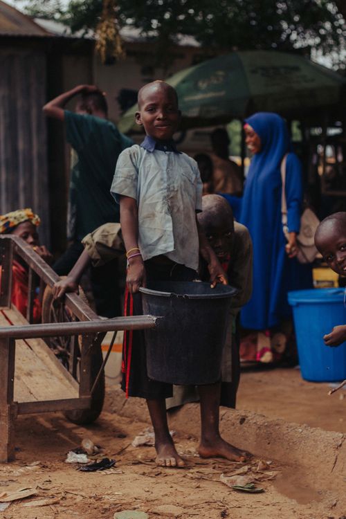 Free Young child carrying water bucket in a lively village setting. Stock Photo