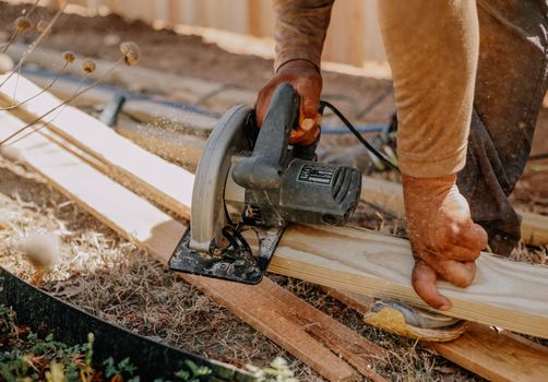 Carpenter operating a circular saw on wooden planks outside, showcasing woodworking skills.