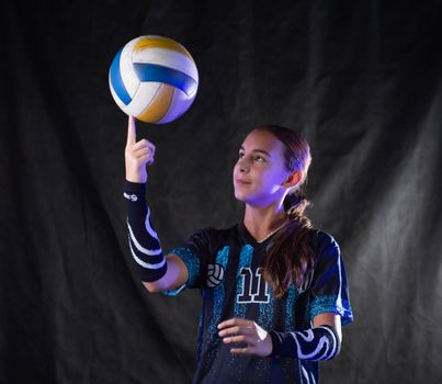 Teen girl skillfully spins a volleyball on her finger in a studio setting.