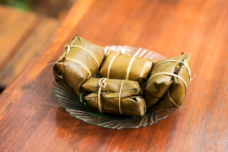 Traditional banana leaf-wrapped snacks on a glass plate set on a wooden table.