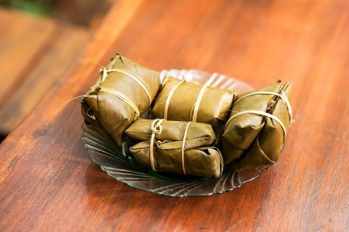 Free Traditional banana leaf-wrapped snacks on a glass plate set on a wooden table. Stock Photo
