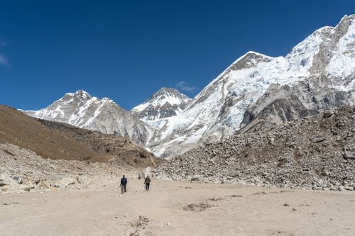 Free Two hikers walk towards rocky Himalayan mountains under clear blue sky. Stock Photo