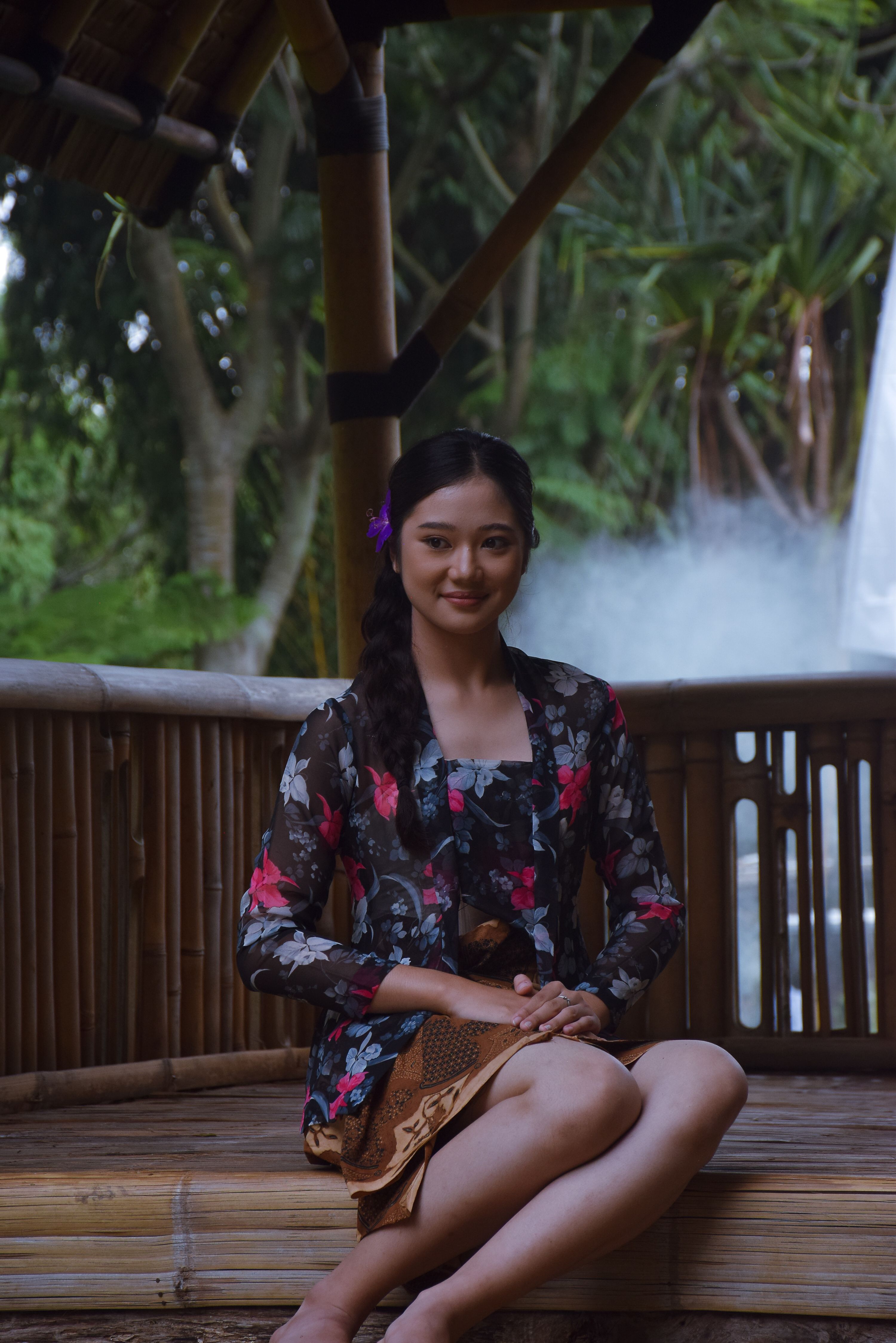 A woman in traditional floral dress sitting outdoors in a bamboo gazebo.