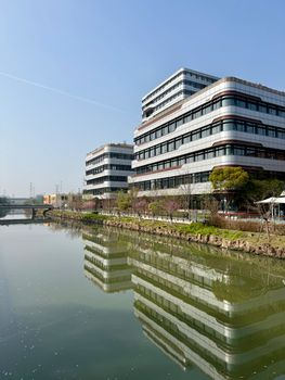 Modern office buildings reflect on calm river in Shanghai's Changning District under clear skies.