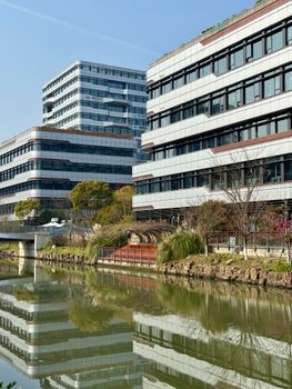 Architectural view of office buildings with reflections in a calm pond, under a clear sky.