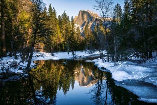 Stunning winter view of Half Dome in Yosemite, reflecting in a serene river.